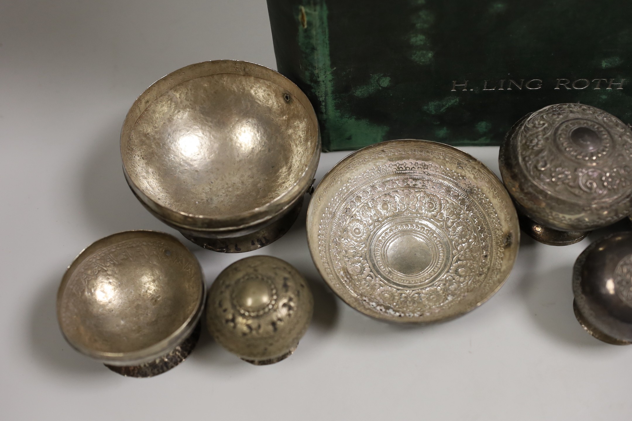 A collection of Malay Straits white metal circular betel nut boxes ('Chimbul'), comprising seven boxes and covers of various sizes (some damaged or missing chain fastenings) and two boxes lacking covers, gross weight 881